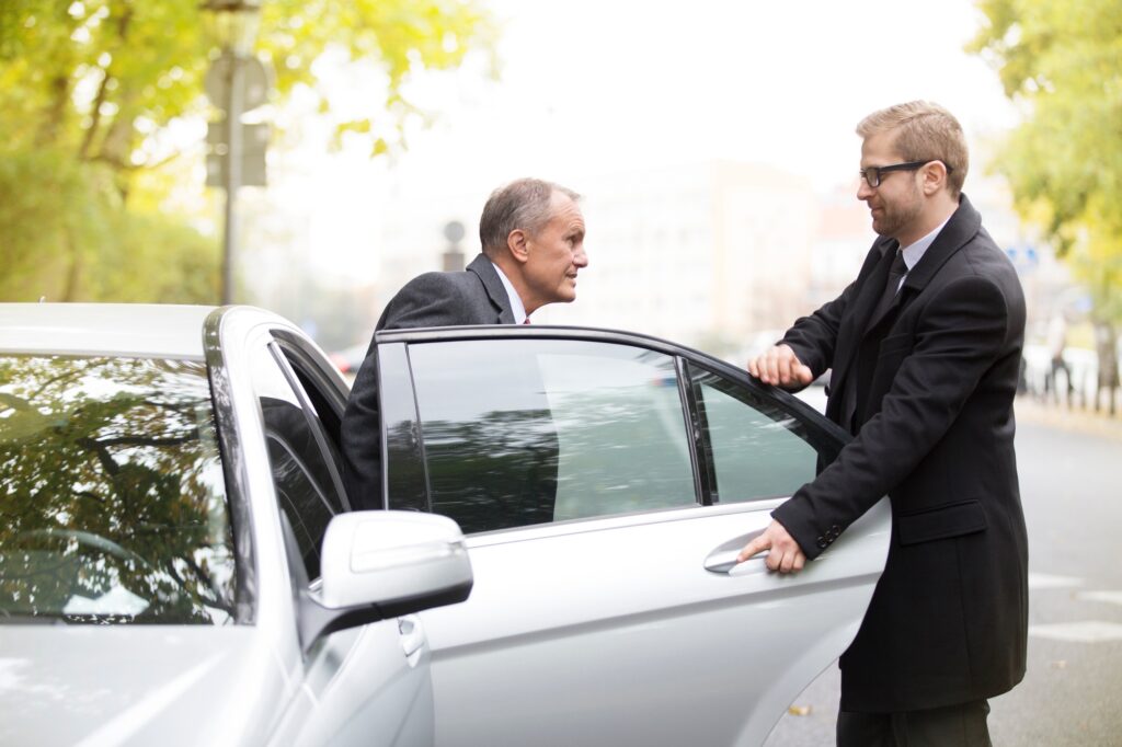 Chauffeur opening car door for businessman getting out