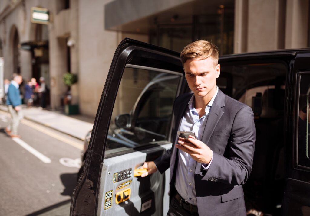 Businessman using smartphone while exiting black cab, London, UK